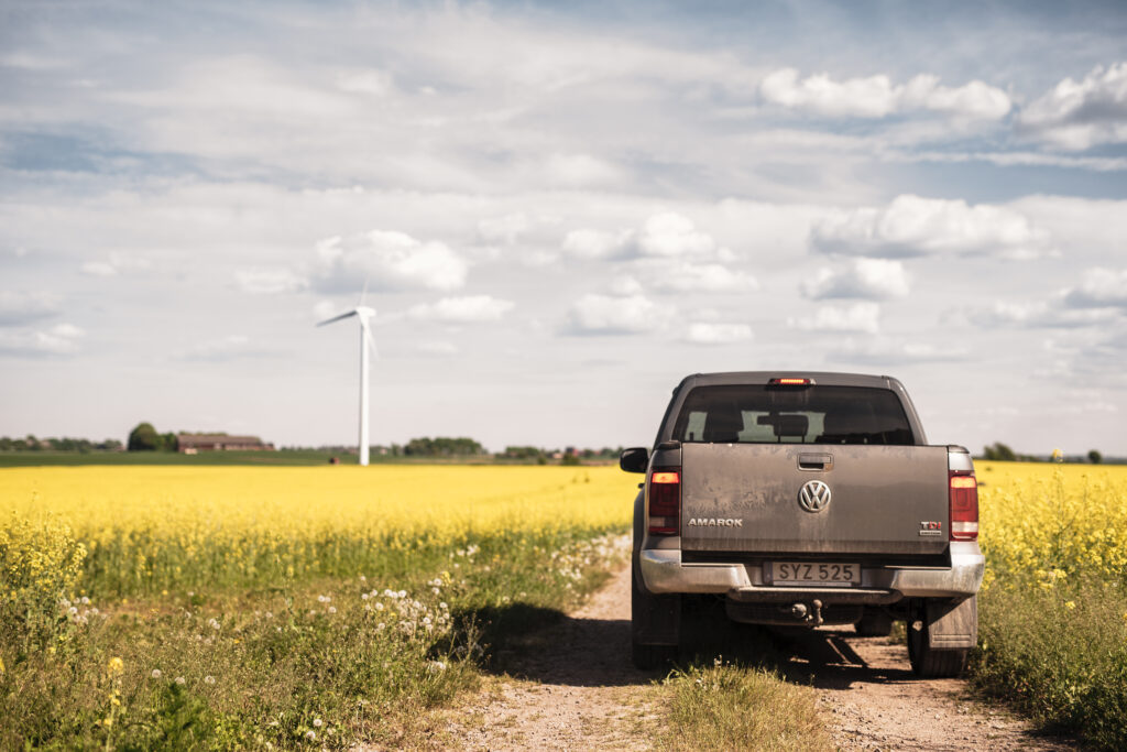 Bil i ett rapsfält med ett vindkraftverk i bakgrunden, använder HVO100 som drivmedel.